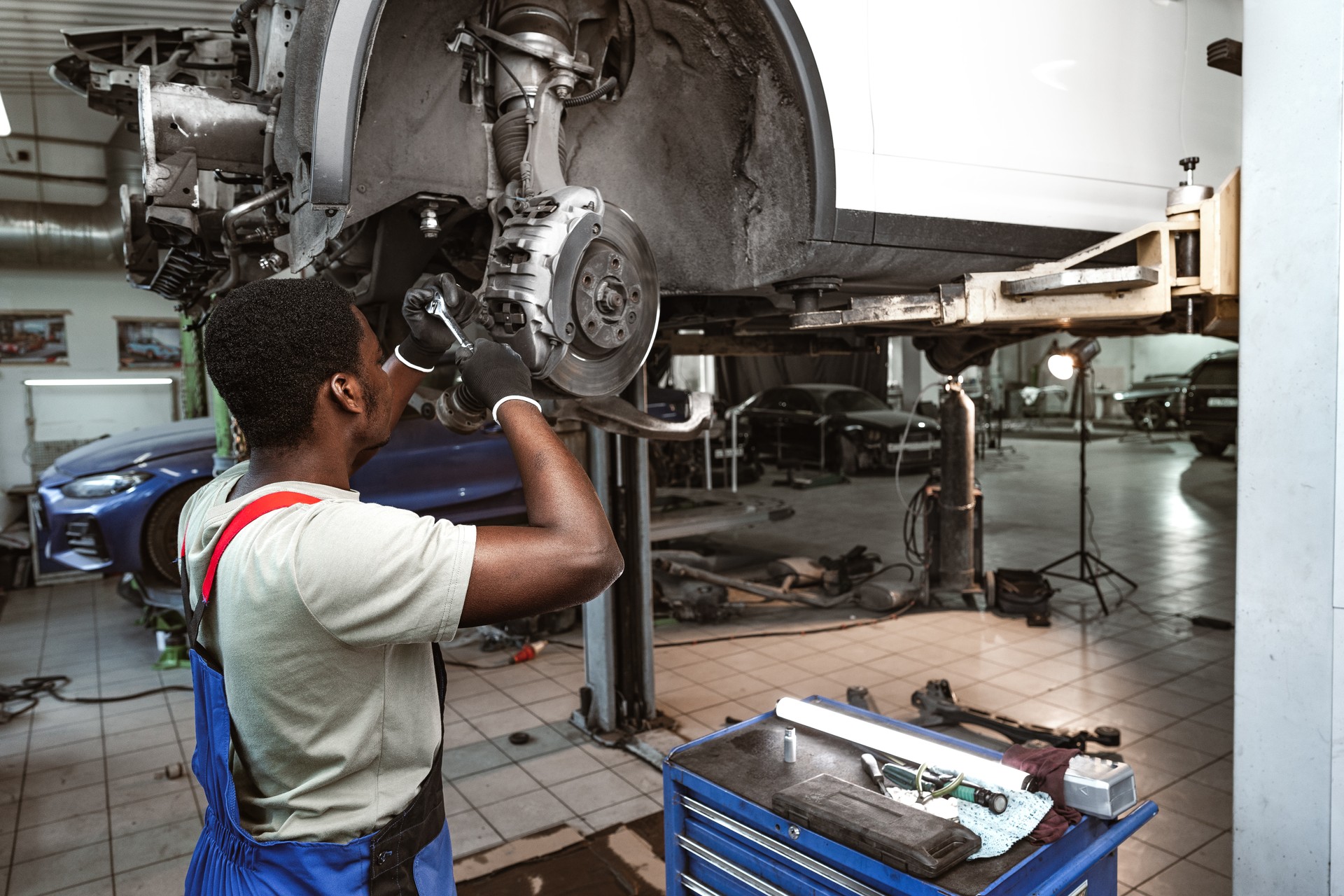 African male auto-mechanic repairing car brakes under the car in auto service